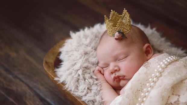 A newborn baby girl sleeps soundly.  She is wearing a tiny golden crown.  A princess is born!