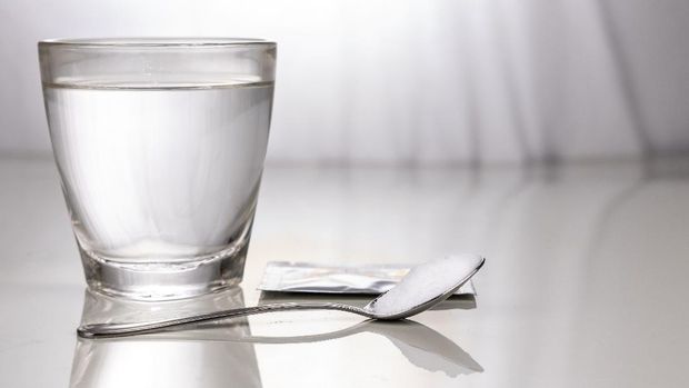 ORS or oral rehydration salt with glass of water, sachet and spoon on table against window light