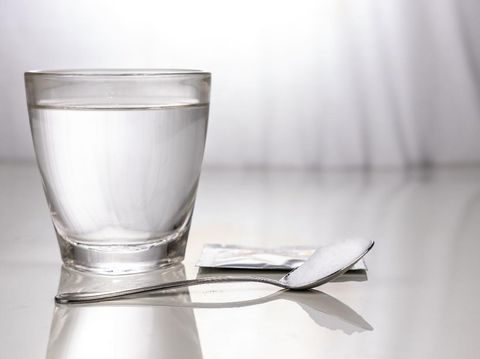 ORS or oral rehydration salt with glass of water, sachet and spoon on table against window light