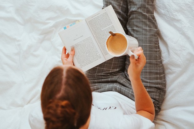 seorang perempuan sedang membaca buku dan minum kopi