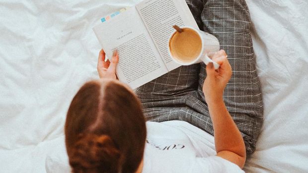 seorang perempuan sedang membaca buku dan minum kopi