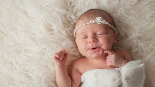 A seven day old newborn baby girl with a cute expression. She is sleeping in a cream colored flokati.