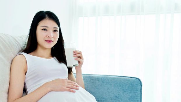 Pregnant woman drinking milk on a sofa
