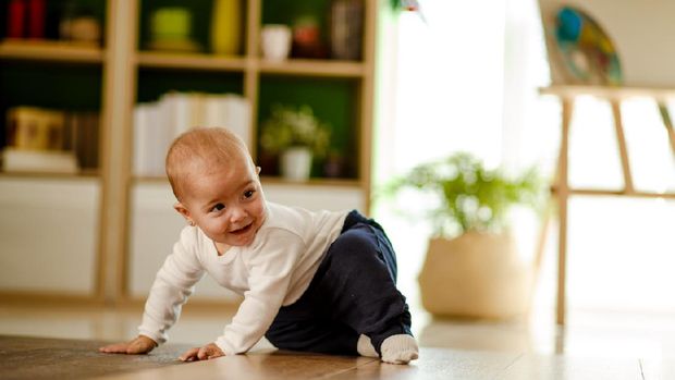 Front view of cute playful baby girl having fun on the floor while being chased by someone.