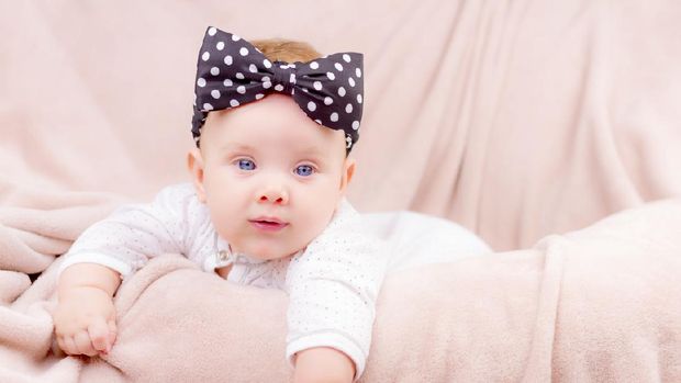 Portrait of a beautiful baby girl with the black band on her head  lying on the sofa