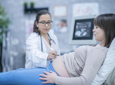 A pregnant woman and her female doctor are indoors in a hospital. The doctor is performing an ultrasound.