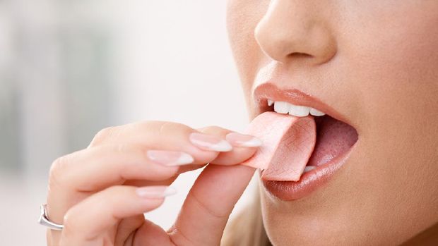 Closeup detail of woman putting pink chewing gum into her mouth.