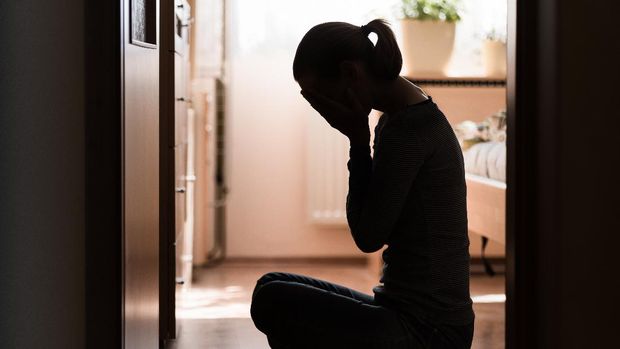 Sad young woman sitting on room floor crying with hand over face