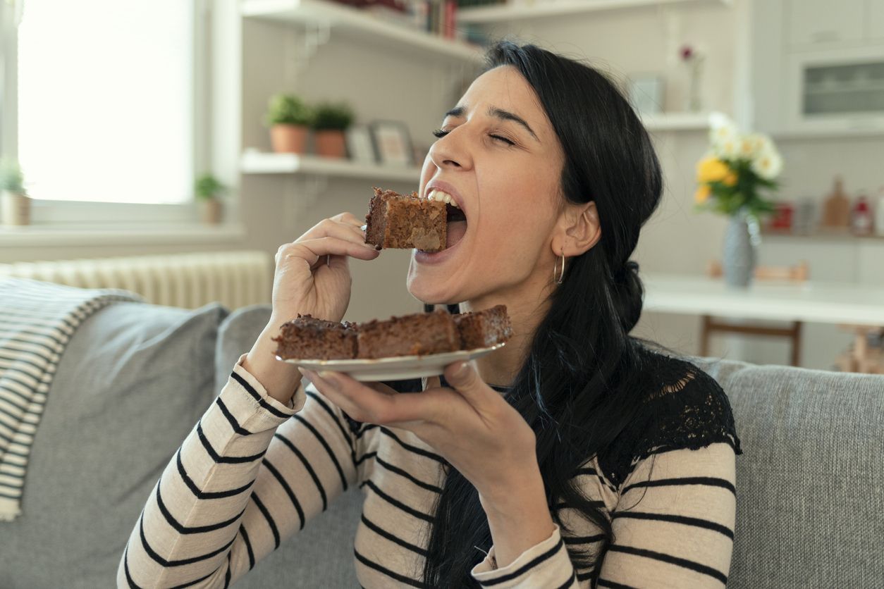 Young Woman Eating Unhealthy Food. Sweetness Indulging and Fattening Concept. Girl Biting Chocolate Cake, High-calorie Sweet Food, Increased Glucose Diabetes. Sweet food addiction.