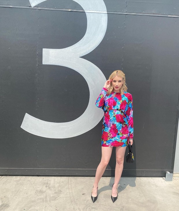 Emma Roberts terlihat sangat cantik saat mengenakan belted dress milik Varsace, dress tersebut dipenuhi dengan motif mawar tie-dye berwarna merah dan biru yang khas.