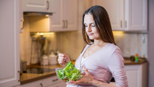 A young beautiful pregnant woman eating a fresh green salad. Healthy nutrition and pregnancy. Pregnant woman's standing in the kitchen with vegetable salad. Healthy lifestyle.