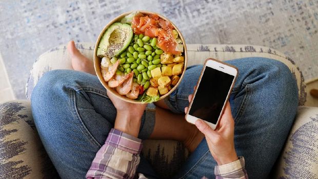 Clean eating diet concept. Vegeterian seafood bowl with smoked salmon, shrimp, avocado in take out paper container in hands of woman having a lunch break. Close up, copy space, top view, background.