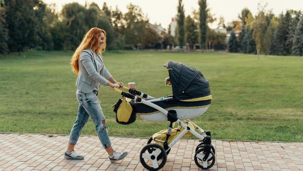 A young mother enjoying the park walk with her little child relaxing in his baby trolley.