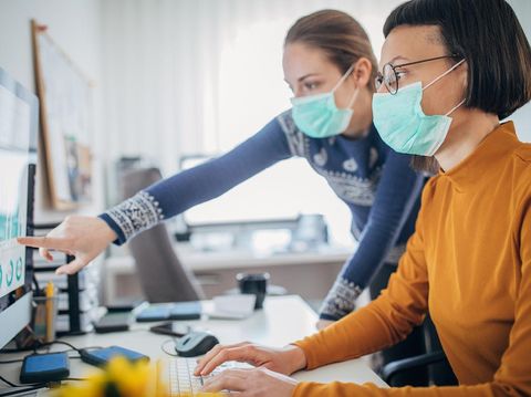Two female colleagues at work wearing face protective mask, to protecting themselves against corona virus