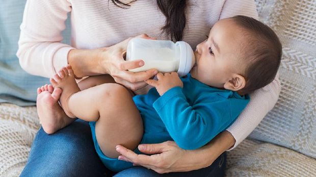 Little infant baby lying on mothers hand drinking milk from bottle. Newborn baby drinking milk from bottle. Cute toddler with milk bottle on leg of mother.