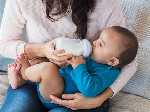 Little infant baby lying on mothers hand drinking milk from bottle. Newborn baby drinking milk from bottle. Cute toddler with milk bottle on leg of mother.