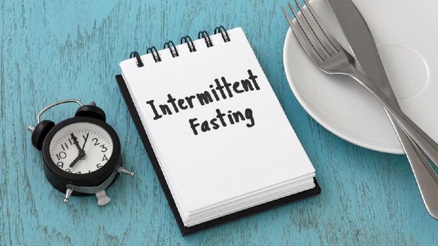 Intermittent fasting word on notepad with clock, fork and knife on white plate, weight loss and diet concept