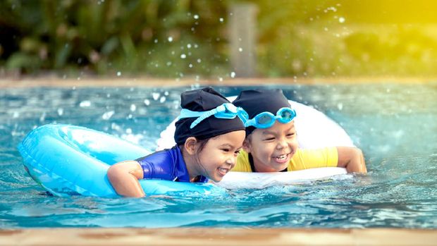 two asian little girls having fun to swim in swimming pool together