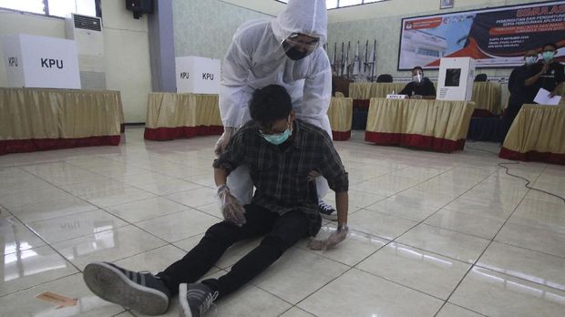 Petugas Kelompok Penyelenggara Pemungutan Suara (KPPS) berpakaian hazmat membantu seorang warga yang pingsan saat simulasi pemungutan dan penghitungan suara Pilkada 2020 di Kantor KPU Kota Surabaya, Jawa Timur, Sabtu (21/11/2020). Simulasi yang diselenggarakan oleh KPU Kota Surabaya dan diikuti perwakilan Panitia Pemilihan Kecamatan (PPK) dan Panitia Pemungutan Suara (PPS) tersebut bertujuan meningkatkan pemahaman serta kemampuan petugas dalam menerapkan protokol kesehatan pada pelaksaaan pemungutan dan penghitungan suara Pilkada 2020 untuk mencegah penyebaran COVID-19. ANTARA FOTO/Moch Asim/hp.