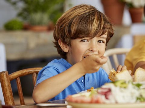 Portrait of boy eating food by table. Male is having lunch at home. He is wearing blue t-shirt.