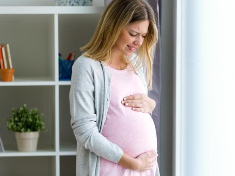 Shot of pregnant young woman feels pain and stomachache and touching her belly at home