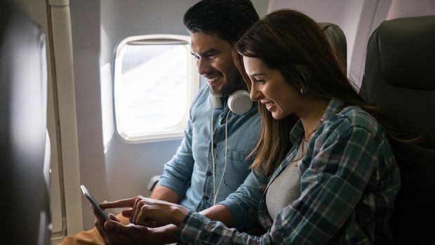 Happy Latin American couple traveling by plane and using their cell phone onboard on airplane mode - lifestyle concepts