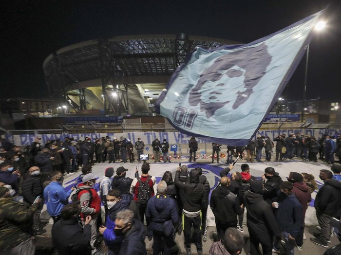 A boy lights a candle as people gather outside the San Paolo Stadium to pay their homage to soccer legend Diego Maradona, in Naples, Italy, Wednesday, Nov. 25, 2020. Diego Maradona has died. The Argentine soccer great was among the best players ever and who led his country to the 1986 World Cup title before later struggling with cocaine use and obesity. He was 60. (AP Photo/Alessandra Tarantino)