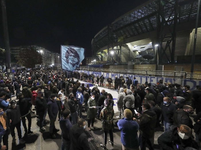 A boy lights a candle as people gather outside the San Paolo Stadium to pay their homage to soccer legend Diego Maradona, in Naples, Italy, Wednesday, Nov. 25, 2020. Diego Maradona has died. The Argentine soccer great was among the best players ever and who led his country to the 1986 World Cup title before later struggling with cocaine use and obesity. He was 60. (AP Photo/Alessandra Tarantino)