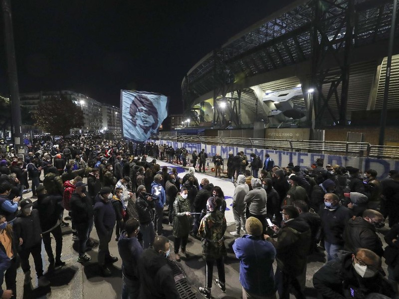 A boy lights a candle as people gather outside the San Paolo Stadium to pay their homage to soccer legend Diego Maradona, in Naples, Italy, Wednesday, Nov. 25, 2020. Diego Maradona has died. The Argentine soccer great was among the best players ever and who led his country to the 1986 World Cup title before later struggling with cocaine use and obesity. He was 60. (AP Photo/Alessandra Tarantino)