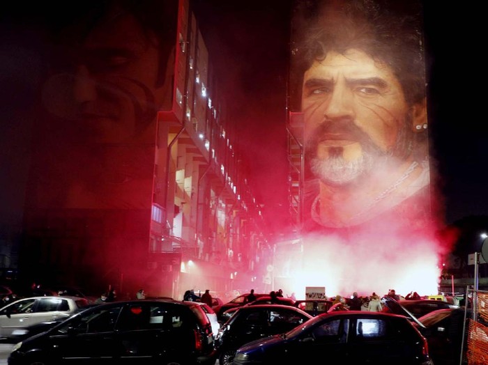 A boy lights a candle as people gather outside the San Paolo Stadium to pay their homage to soccer legend Diego Maradona, in Naples, Italy, Wednesday, Nov. 25, 2020. Diego Maradona has died. The Argentine soccer great was among the best players ever and who led his country to the 1986 World Cup title before later struggling with cocaine use and obesity. He was 60. (AP Photo/Alessandra Tarantino)