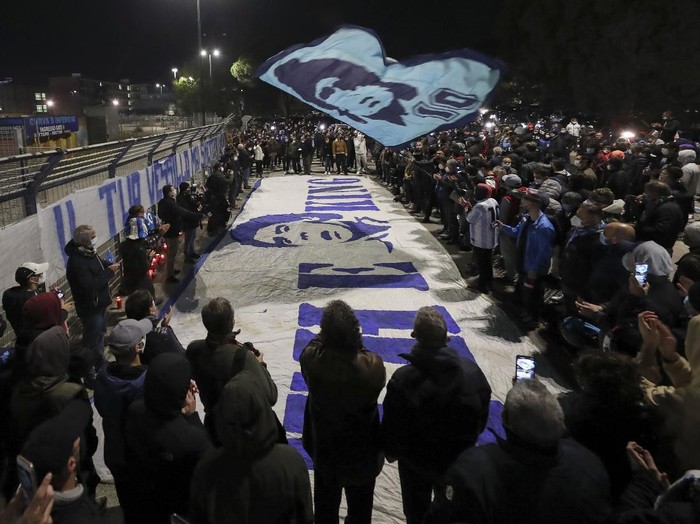A boy lights a candle as people gather outside the San Paolo Stadium to pay their homage to soccer legend Diego Maradona, in Naples, Italy, Wednesday, Nov. 25, 2020. Diego Maradona has died. The Argentine soccer great was among the best players ever and who led his country to the 1986 World Cup title before later struggling with cocaine use and obesity. He was 60. (AP Photo/Alessandra Tarantino)