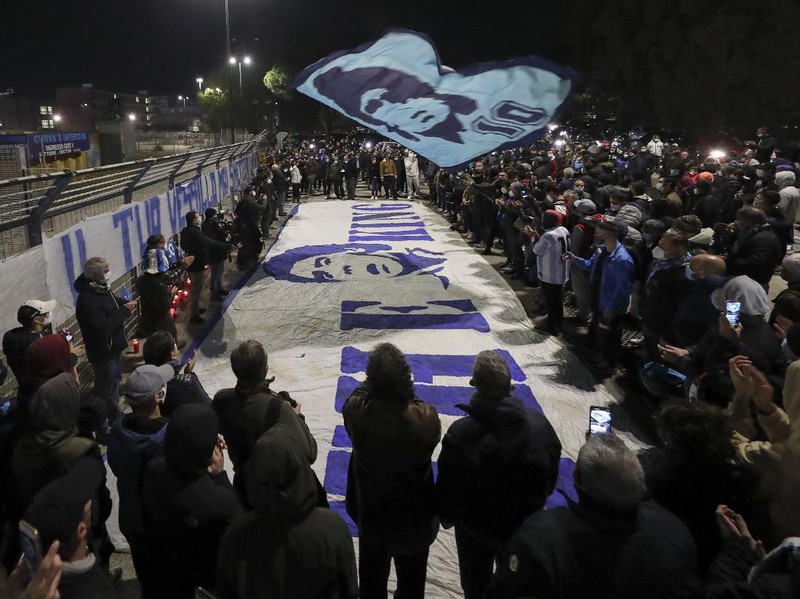 A boy lights a candle as people gather outside the San Paolo Stadium to pay their homage to soccer legend Diego Maradona, in Naples, Italy, Wednesday, Nov. 25, 2020. Diego Maradona has died. The Argentine soccer great was among the best players ever and who led his country to the 1986 World Cup title before later struggling with cocaine use and obesity. He was 60. (AP Photo/Alessandra Tarantino)