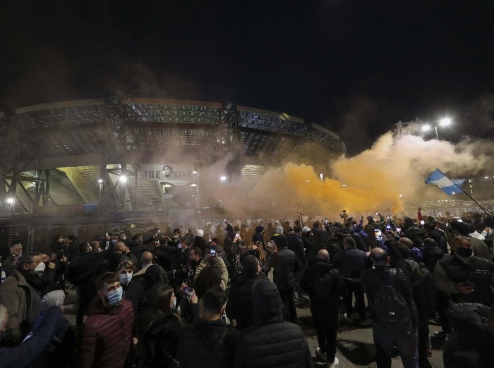 A boy lights a candle as people gather outside the San Paolo Stadium to pay their homage to soccer legend Diego Maradona, in Naples, Italy, Wednesday, Nov. 25, 2020. Diego Maradona has died. The Argentine soccer great was among the best players ever and who led his country to the 1986 World Cup title before later struggling with cocaine use and obesity. He was 60. (AP Photo/Alessandra Tarantino)