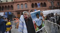 Seorang warga mengusap air mata di wajahnya sembari membawa foto Maradona saat mendatangi area istana kepresidenan Argentina. AP Photo/Rodrigo Abd.