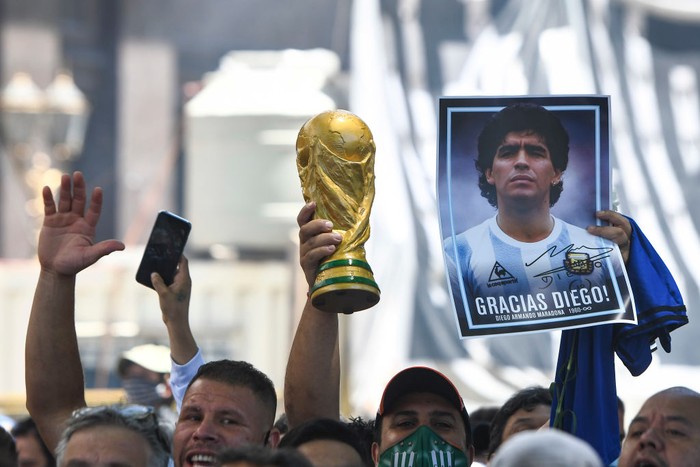 BUENOS AIRES, ARGENTINA - NOVEMBER 26:  A fans holds a photograph of Diego Maradona and a replica of the world cup trophy as he queues to enter the government palace on November 26, 2020 in Buenos Aires, Argentina. Maradona died of a heart attack at his home on Thursday 25 aged 60 . He is considered among the best footballers in history and lead his national team to the World Cup in 1986. President of Argentina Alberto Fernandez declared three days of national mourning. (Photo by Rodrigo Valle/Getty Images)