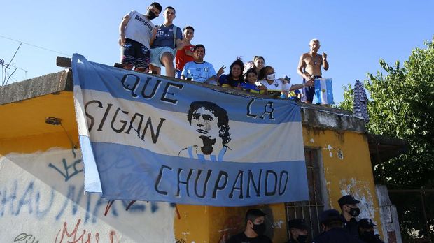Fans stand on a roof of a house along the way of the motorcade carrying the remains of Diego Maradona to the Jardin de Bellavista cemetery in Buenos Aires, Argentina, Thursday, Nov. 26, 2020. The Argentine soccer great who was among the best players ever and who led his country to the 1986 World Cup title died from a heart attack at his home Wednesday, at the age of 60. (AP Photo/Maria Paula Avila)