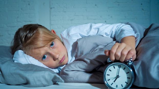 Sweet sleepless little girl lying sad in bed looking at alarm clock having to wake up but feeling tired sleepless in Troubles staying asleep Night Terrors Sleep disorder and Children Insomnia concept.