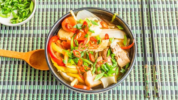 Suan cai - traditional Chinese stew of pork and pickled Chinese cabbage in a black bowl on a bamboo napkin.