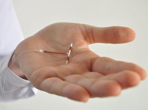 Holding an IUD birth control copper coil device in hand, used for contraception - side view