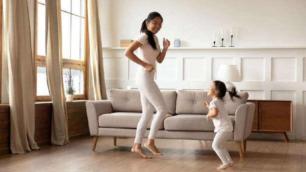 Overjoyed young Asian mom and cute little biracial daughter have fun dancing in living room together, happy millennial mother play involved in funny activity with small Vietnamese girl child at home