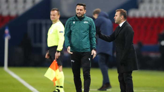 Basaksehirs manager Okan Buruk, right, reacts next to Romanian 4th referee Sebastian Coltescu during the Champions League group H soccer match between Paris Saint Germain and Istanbul Basaksehir at the Parc des Princes stadium in Paris, Tuesday Dec. 8 , 2020. (AP Photo/Francois Mori)