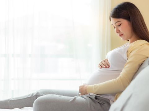 Happy pregnant mother touching and looking beautiful belly sitting on cozy bed at home. prenatal, pregnancy, motherhood, expect concept. Young pregnance girl care and love her baby. copy space