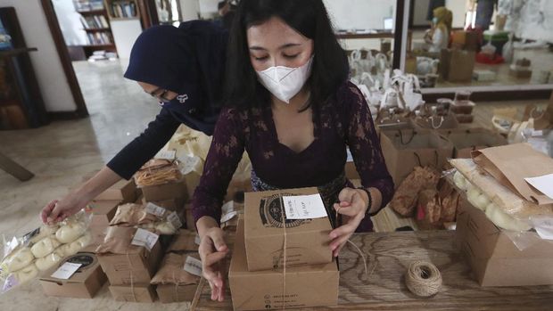 Reny Ajeng, center, one of the organizers of Pahingan Sunday Market, packs food made by tenants to shipped to customers in Jakarta, Indonesia, Sunday, Nov. 29, 2020. Ajeng helps to organize Pahingan Sunday Market, an online event run by Omah Wulangreh, an art and cultural community in Jakarta, that provides online space for sellers and for buyers to preorder items like traditional snacks, batik clothes, or coffee, to help people to have extra income during the COVID-19 pandemic. (AP Photo/Achmad Ibrahim)