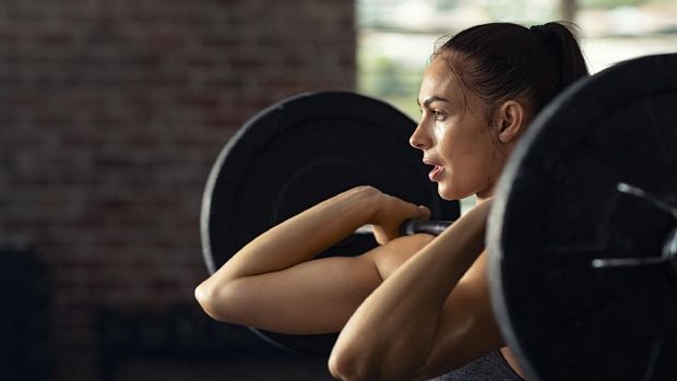 Fitness woman doing shoulder press exercise with a weight bar at cross training gym. Muscular woman in gym doing heavy weight exercises. Concentrated athlete doing barbell lifting at health club with copy space.