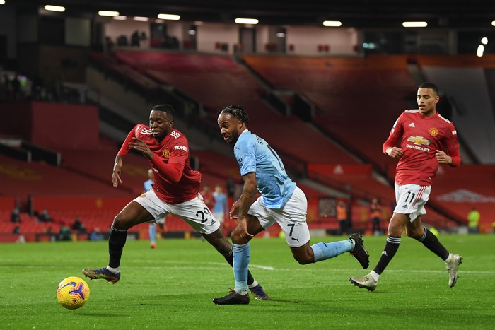 MANCHESTER, ENGLAND - DECEMBER 12: Raheem Sterling of Manchester City  runs with the ball at Aaron Wan-Bissaka of Manchester United as Mason Greenwood looks on during the Premier League match between Manchester United and Manchester City at Old Trafford on December 12, 2020 in Manchester, England. The match will be played without fans, behind closed doors as a Covid-19 precaution. (Photo by Michael Regan/Getty Images)