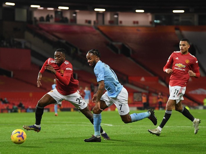 MANCHESTER, ENGLAND - DECEMBER 12: Raheem Sterling of Manchester City  runs with the ball at Aaron Wan-Bissaka of Manchester United as Mason Greenwood looks on during the Premier League match between Manchester United and Manchester City at Old Trafford on December 12, 2020 in Manchester, England. The match will be played without fans, behind closed doors as a Covid-19 precaution. (Photo by Michael Regan/Getty Images)