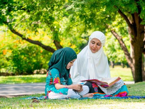 Muslim mother teach her daughter to read religion textbook for understanding the way of good life. They stay in the green garden during day time.