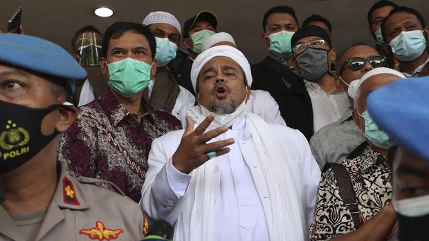 Indonesian Islamic cleric and the leader of Islamic Defenders Front Rizieq Shihab, center, is escorted by officers and lawyers upon arrival at the regional police headquarters in Jakarta, Indonesia. Saturday, Dec. 12, 2020. The firebrand cleric turned himself in to the police after he was accused of inciting people to breach pandemic restrictions by holding events with large crowds. Shihab arrived at Jakarta police headquarters a day after police warned they would arrest him after he ignored several summonses. (AP Photo/Achmad Ibrahim)