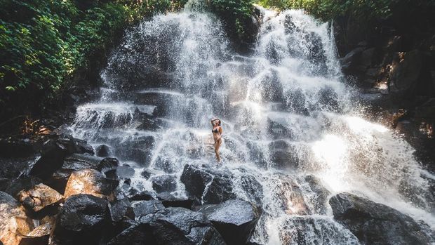 Air Terjun Kanto Lampo di Bali Woman enjoying under stream of big and beautiful cascade waterfall. Girl with slim body and long hair. Kanto Lampo in Ubud area