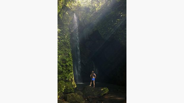 Air Terjun Pengempu Young woman travel in Bali rainforest. Happy girl enjoy jungle nature. Stand in natural pool under waterfall, see on falling water. Walking day tour, hiking activity adventure on family summer holiday
